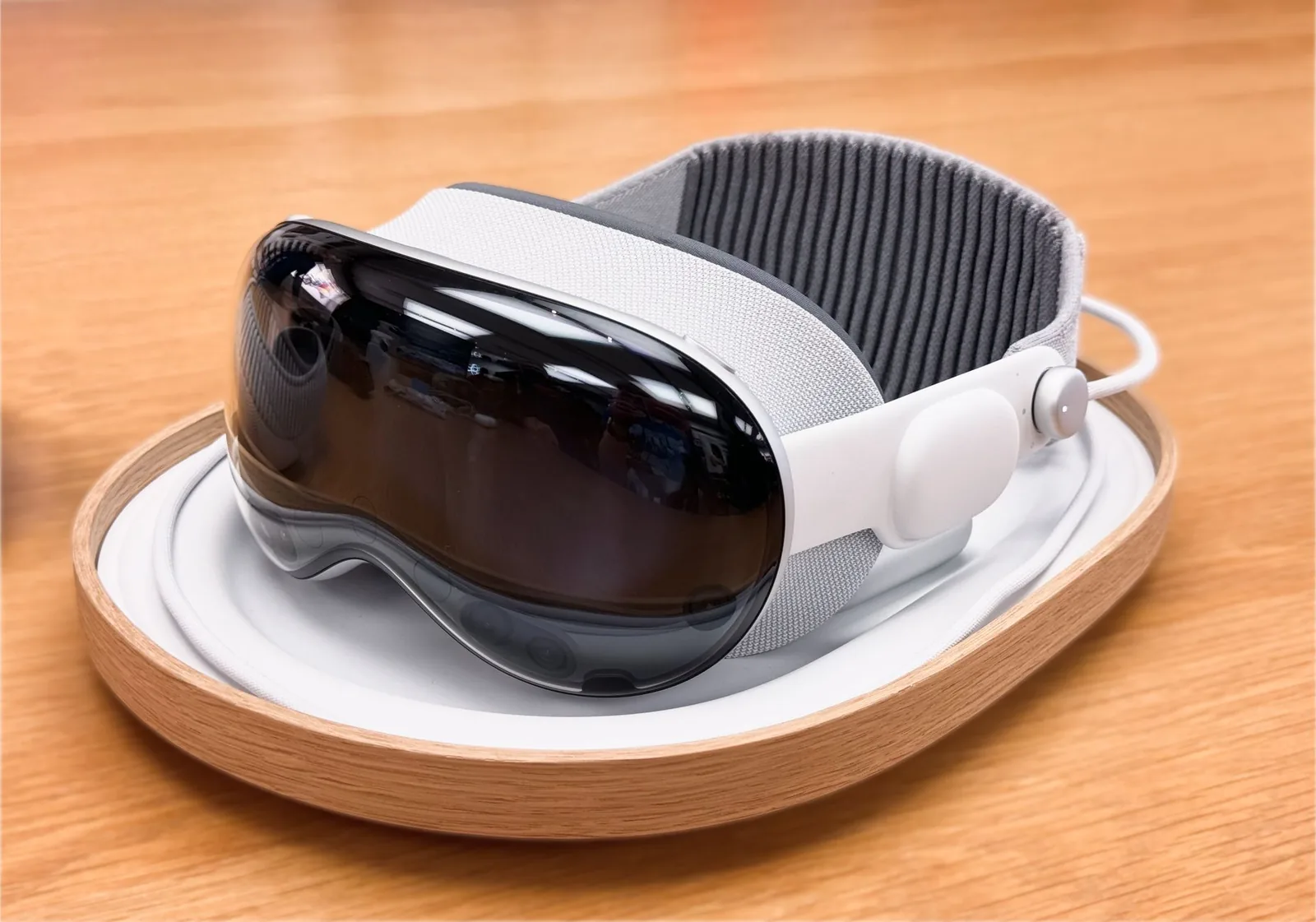 Apple Vision Pro-ის თეთრი შერეული რეალობის ჰედსეტი ხის ლანგარზე დევს.