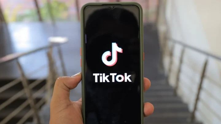 ხელში დაჭერილ სმარტფონის ეკრანზე TikTok-ის ლოგო და სახელწოდება ჩანს.
