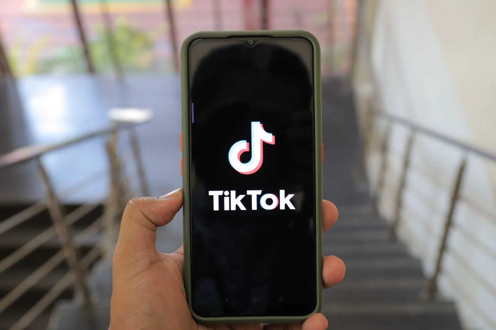 ხელში დაჭერილ სმარტფონის ეკრანზე TikTok-ის ლოგო და სახელწოდება ჩანს.